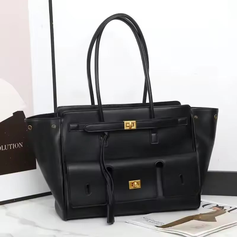 Black leather-look tote bag with two top handles, front pockets and gold clasps, shown on a white surface