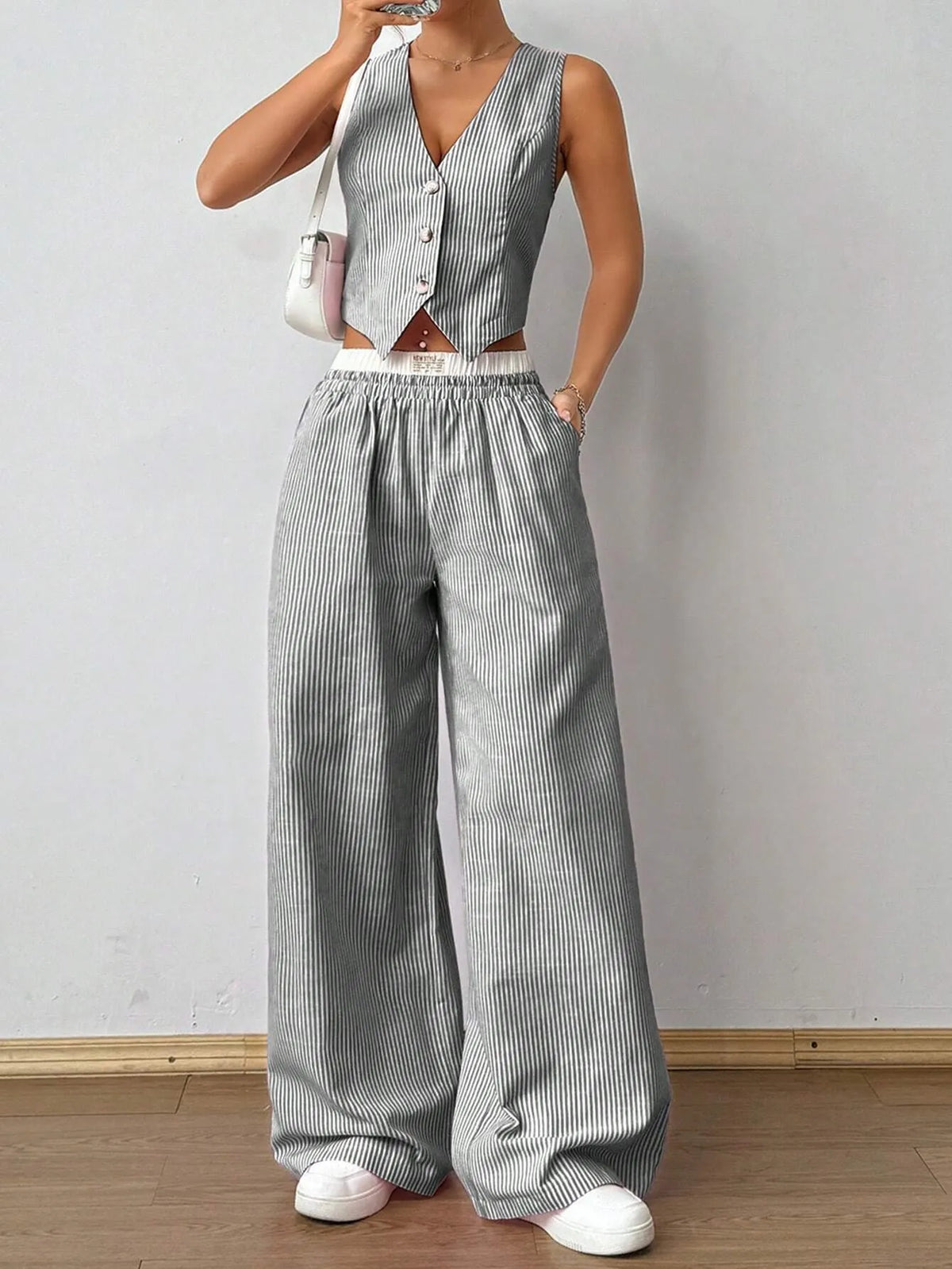 Woman in a grey pinstripe V-neck vest top and matching wide-leg pants with white sneakers, front view