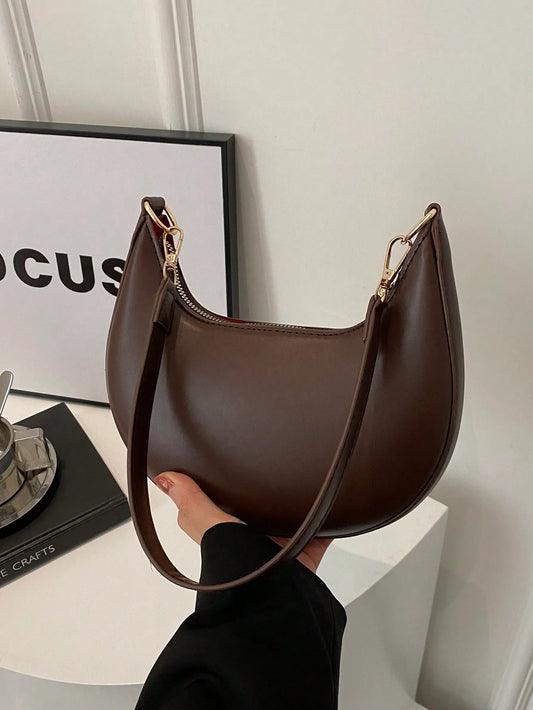 Dark brown half-moon shoulder bag with a gold clasp, held in one hand