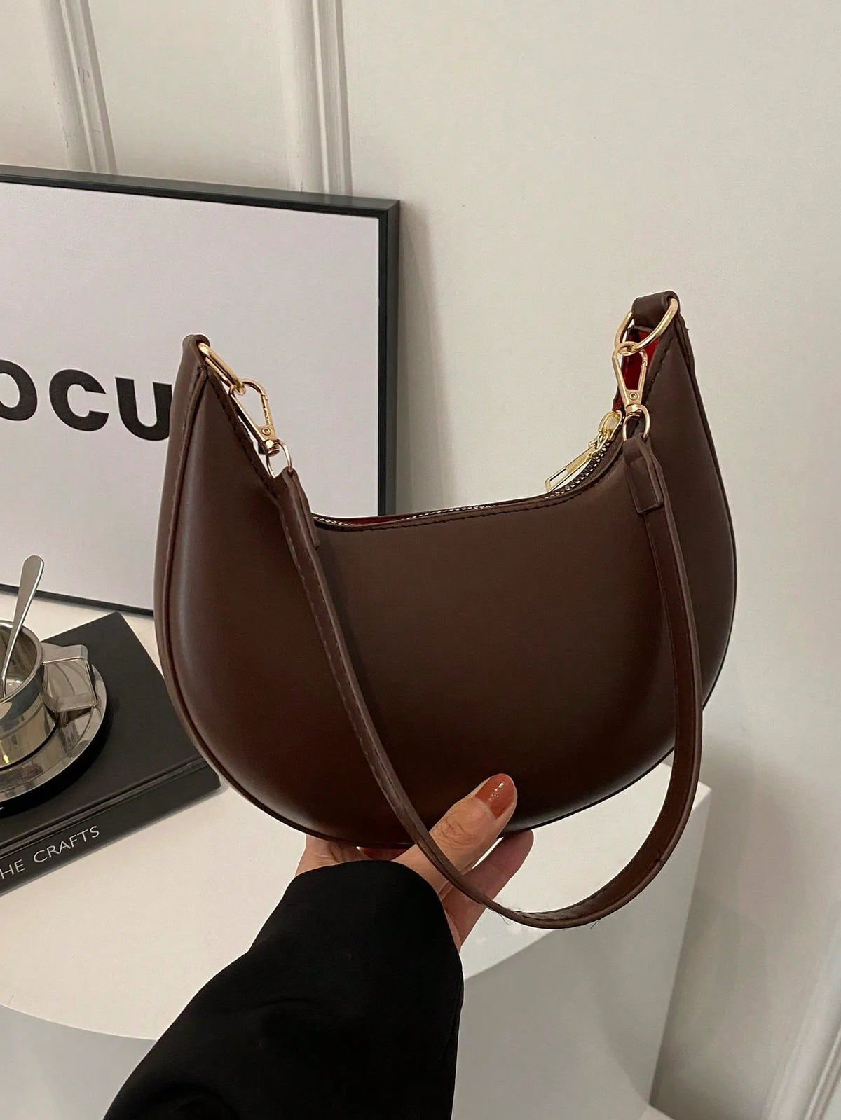 Dark brown half-moon shoulder bag held by its strap, side view