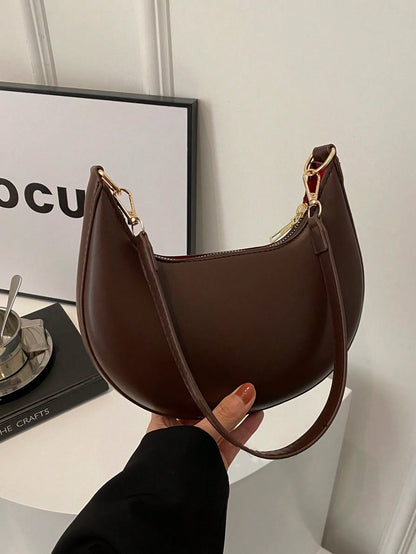 Dark brown half-moon shoulder bag held by its strap, side view