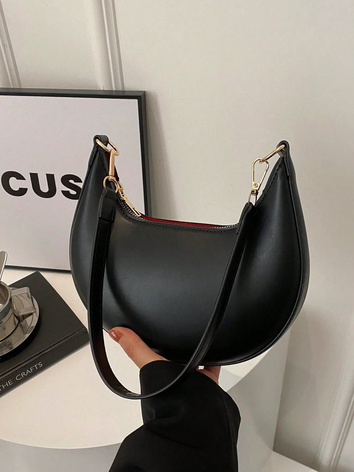 Black half-moon shoulder bag with a gold clasp, held in one hand