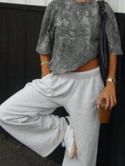 Woman wearing an oversized grey camo print T-shirt with light grey sweatpants, one leg raised
