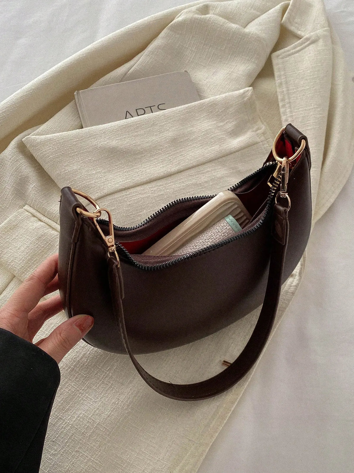 Dark brown half-moon bag with the top open to show the lining and a card inside
