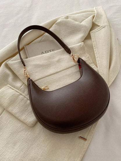 Dark brown half-moon shoulder bag with a looped strap, laid on a cream cloth