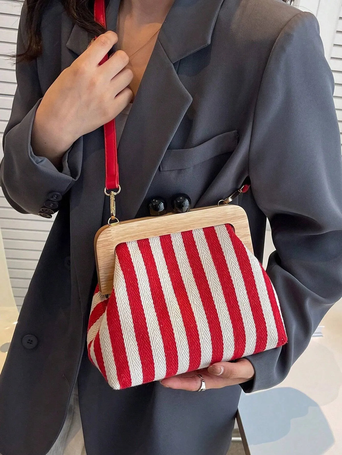 Woman wearing a grey blazer with a red and cream striped crossbody bag with a wooden frame