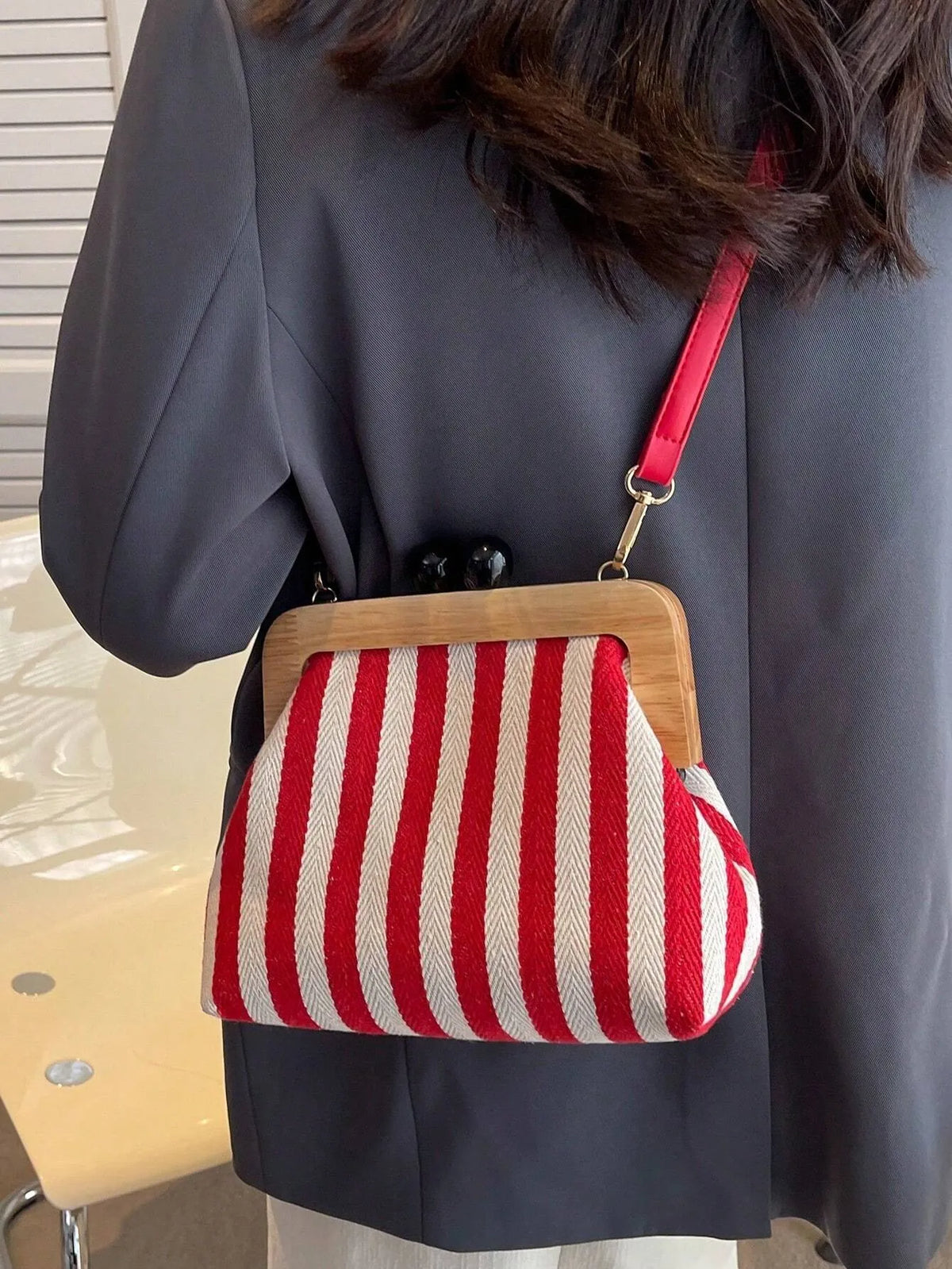 Red and cream striped crossbody bag with a wooden frame worn over a grey blazer, side view
