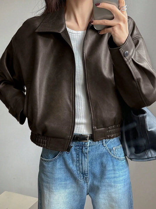 Woman in a cropped dark brown leather-look jacket over a white top and light-wash jeans, taking a mirror selfie