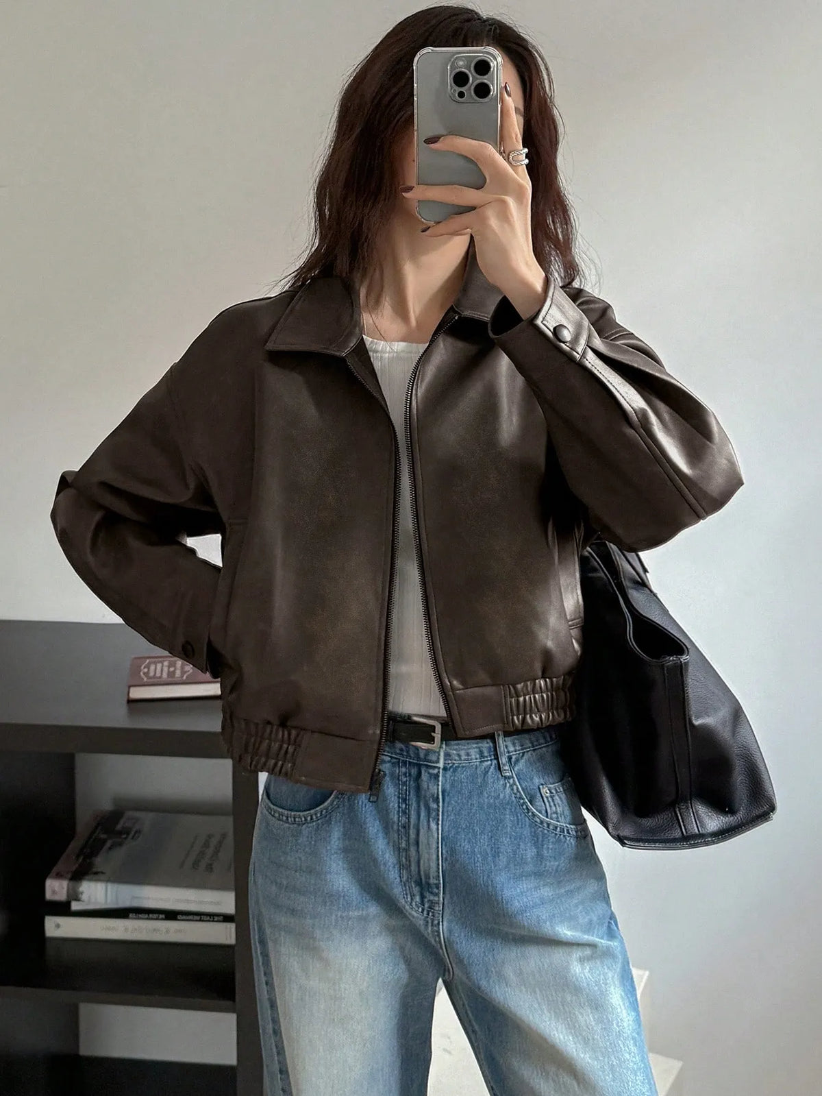 Front view of the cropped dark brown leather-look jacket over a white top and jeans, mirror selfie