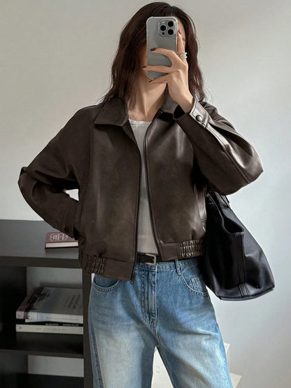 Front view of the cropped dark brown leather-look jacket over a white top and jeans, mirror selfie