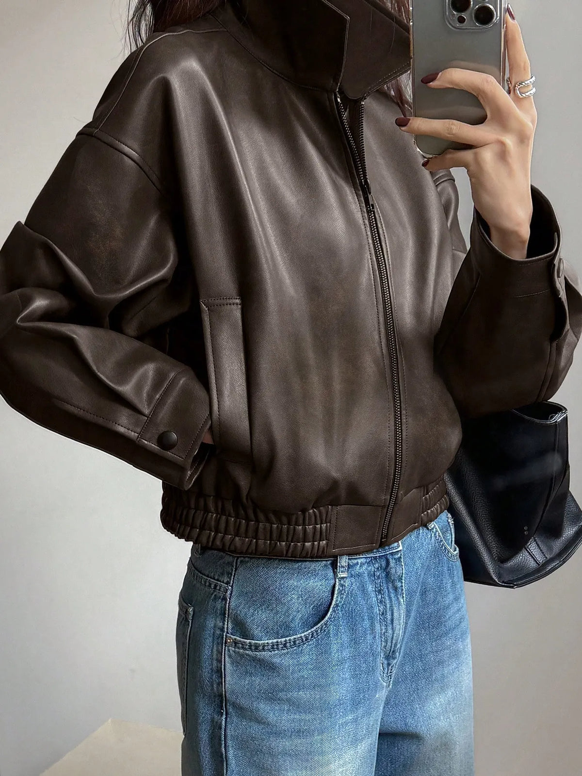 Side view of the cropped dark brown leather-look jacket with an elastic hem, taking a mirror selfie