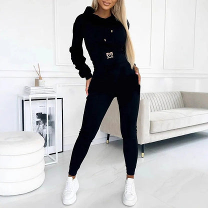 Woman wearing a black hooded long-sleeve top with a buckle detail at the waist and matching black pants with white sneakers