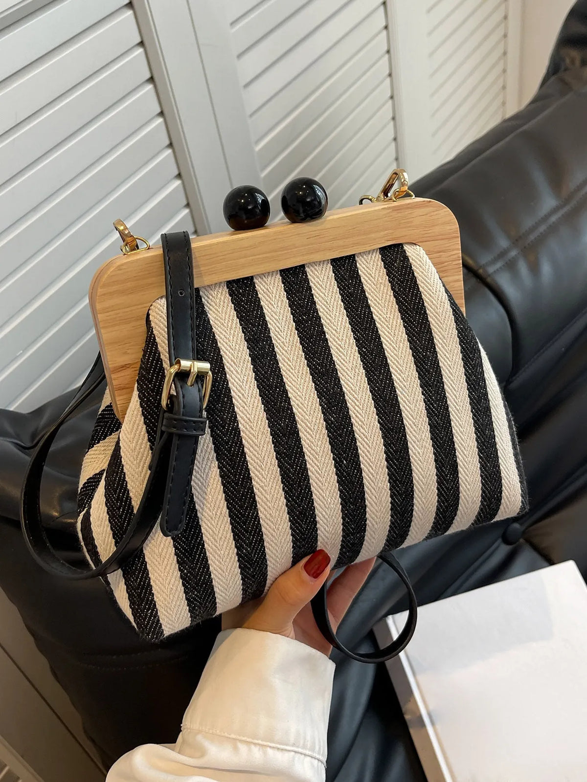 Black and cream striped bag with a wooden clasp frame and black strap, held in one hand
