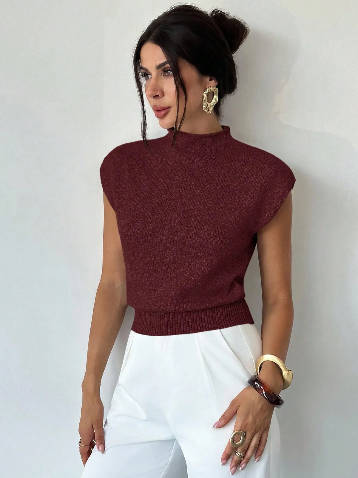 Woman wearing a burgundy high-neck cap-sleeve knit top with white trousers