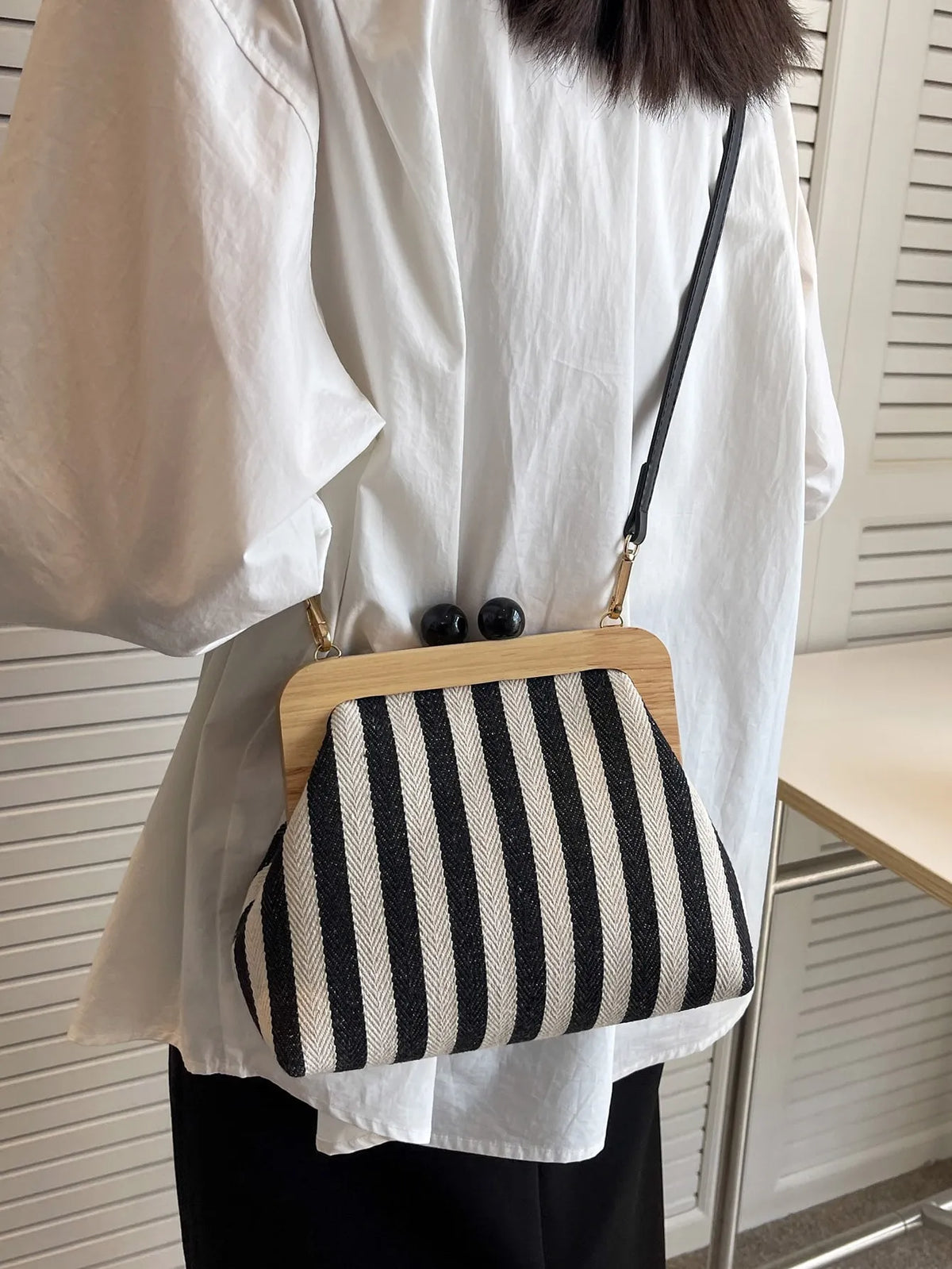 Black and cream striped crossbody bag with a wooden frame worn over a white shirt