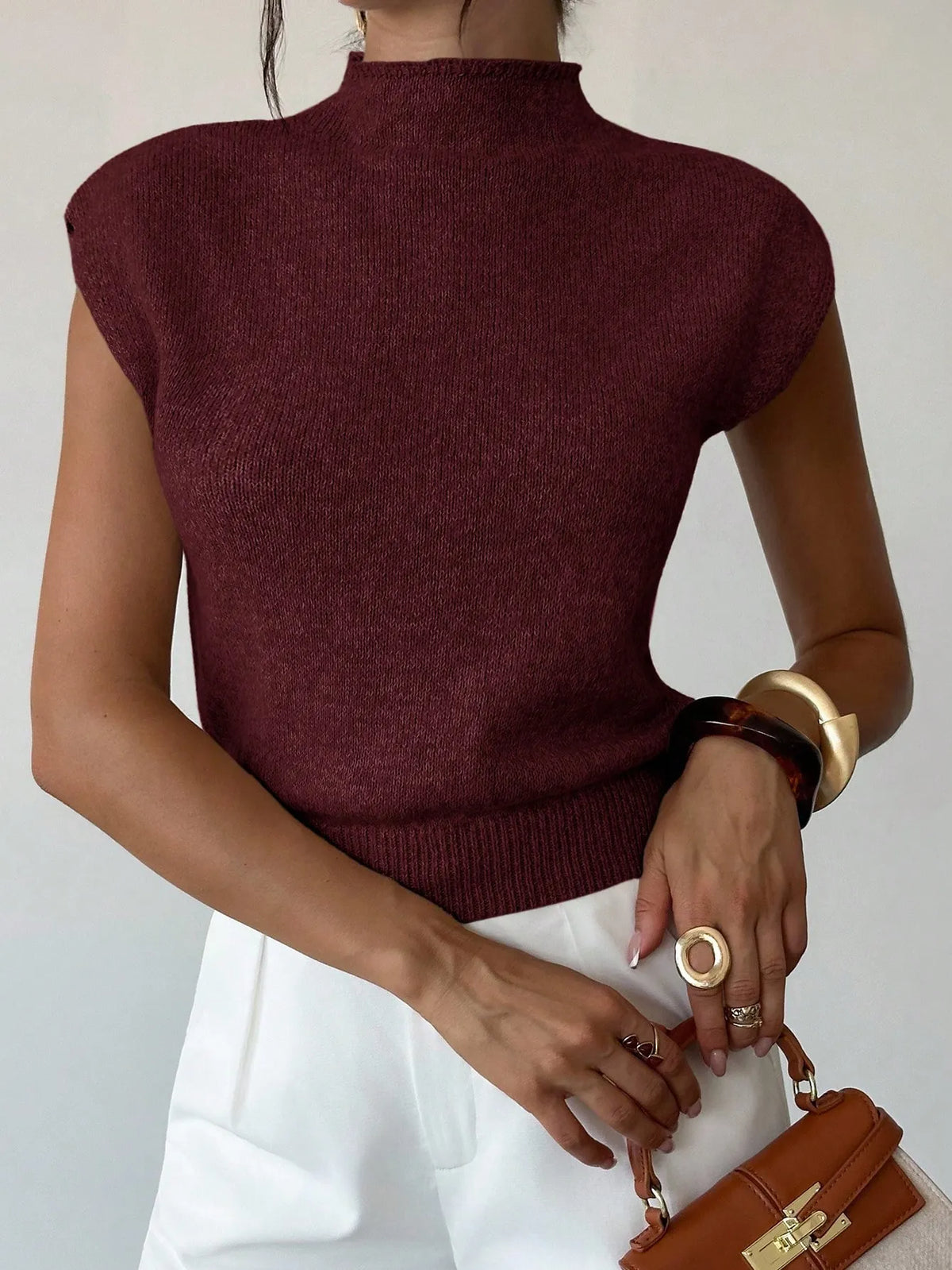 Close view of the burgundy high-neck knit top with white trousers and a brown handbag