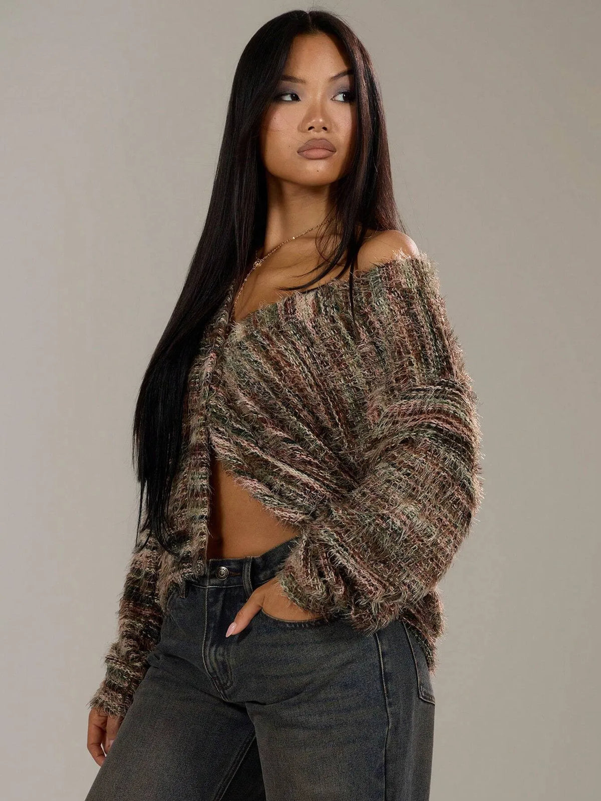 Woman in the brown striped oversized knit cardigan with her hands in her jeans pockets, three-quarter view