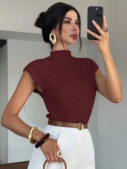 Woman in the burgundy high-neck knit top and white trousers taking a mirror selfie