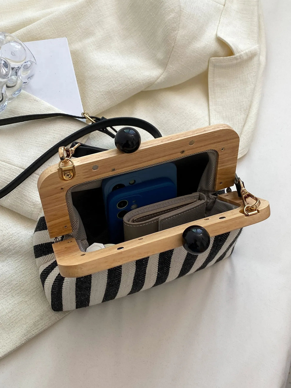 Open black and cream striped bag with a wooden frame showing a phone and cards inside
