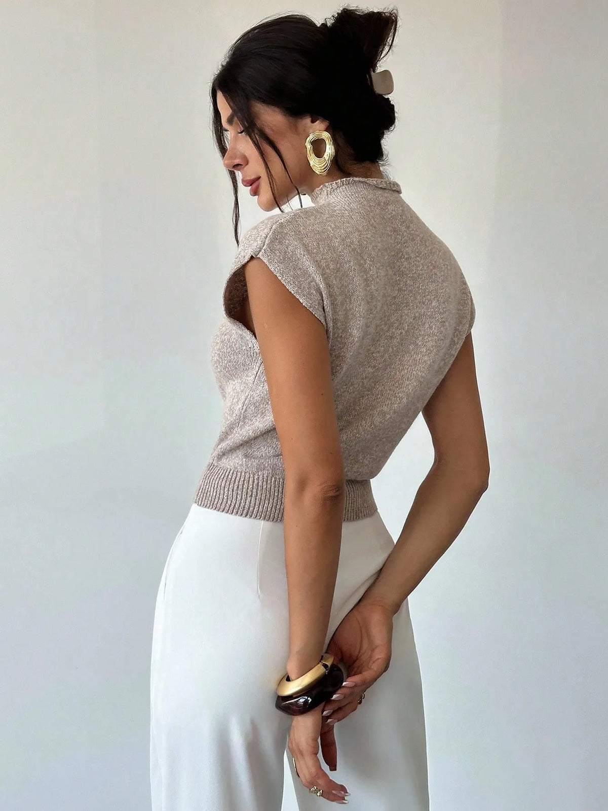 Side view of the beige high-neck cap-sleeve knit top with white trousers