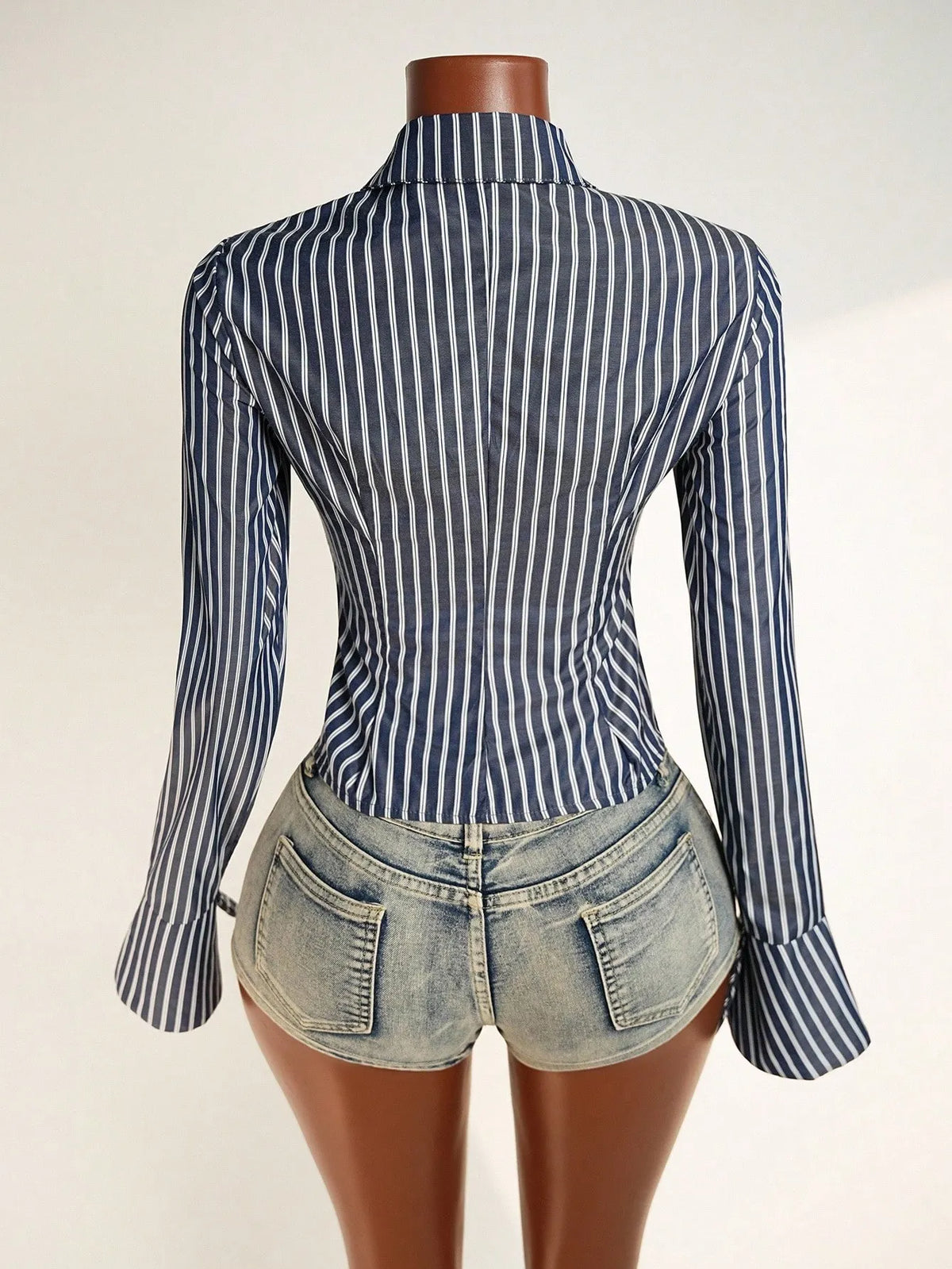 Back view of the navy and white pinstripe crop shirt on a mannequin with distressed denim shorts