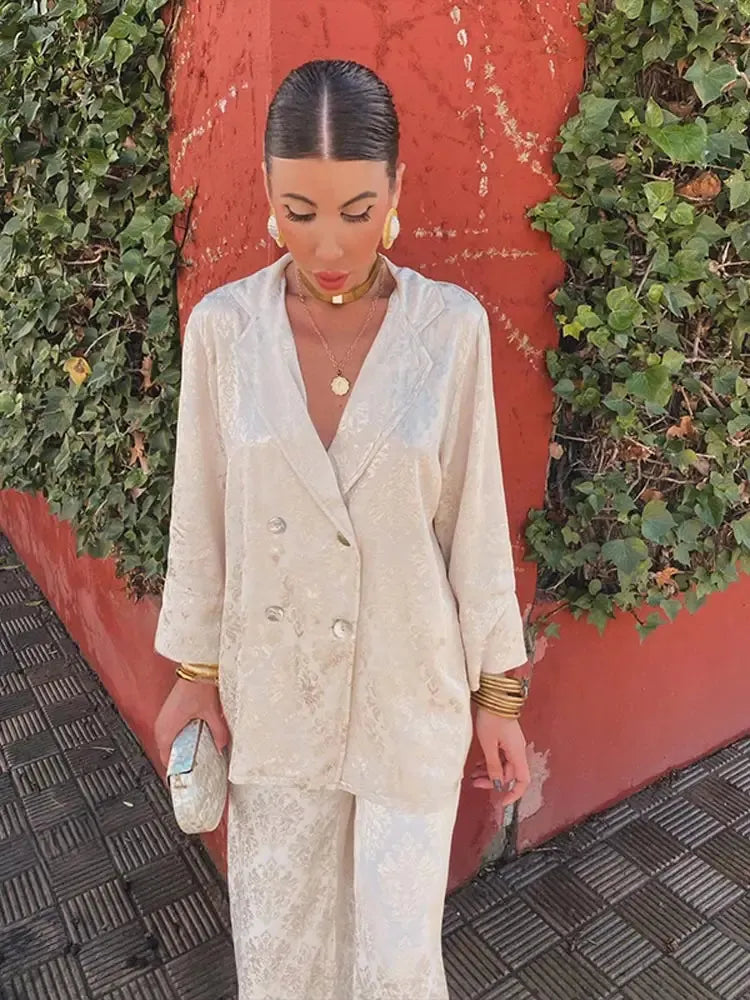 Woman wearing a cream patterned double-breasted V-neck blazer and matching pants, front view holding a small clutch