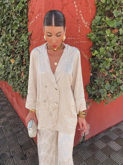 Woman wearing a cream patterned double-breasted V-neck blazer and matching pants, front view holding a small clutch