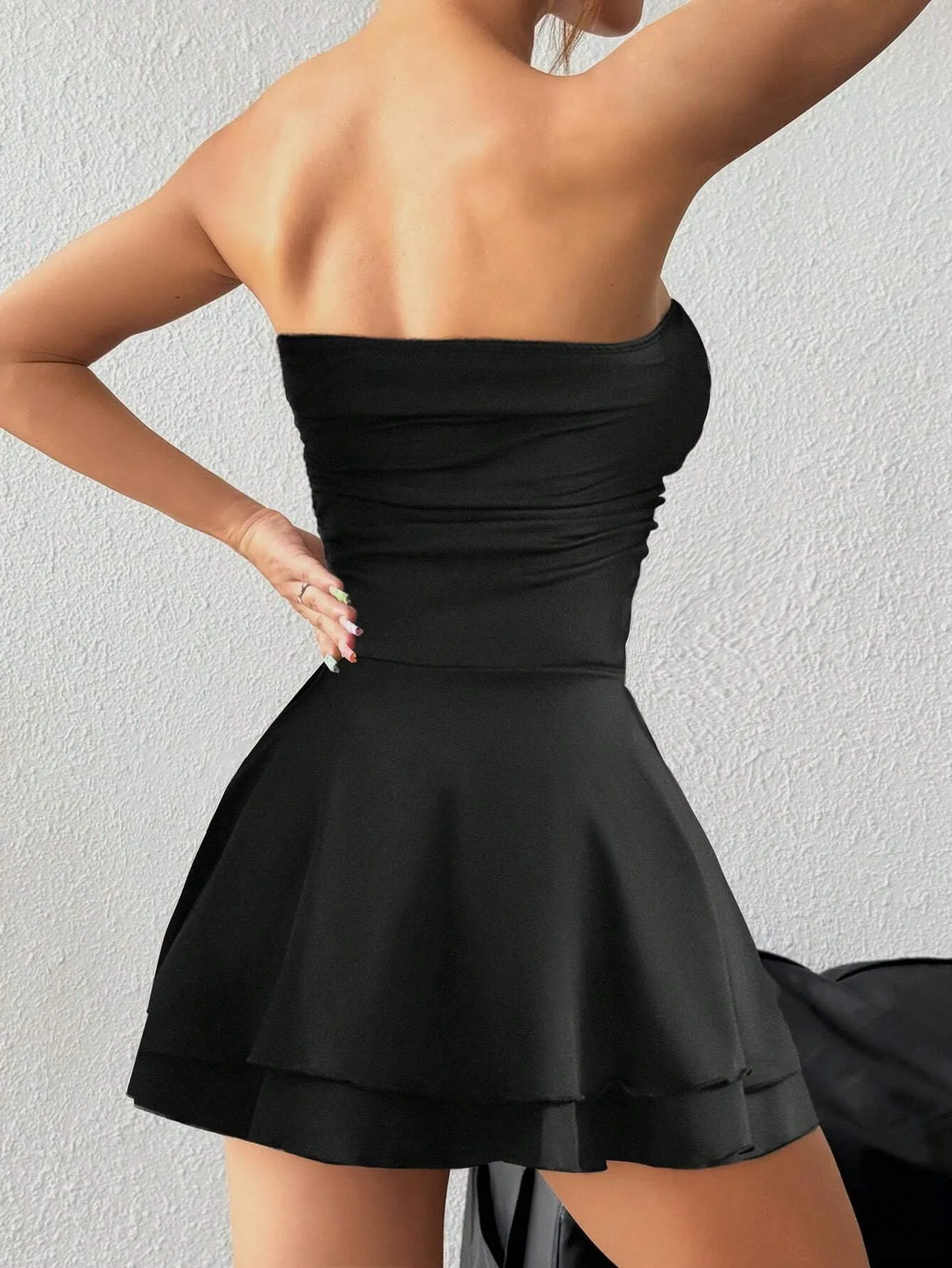 Black ruched strapless mini dress with a flared skirt, three-quarter back view