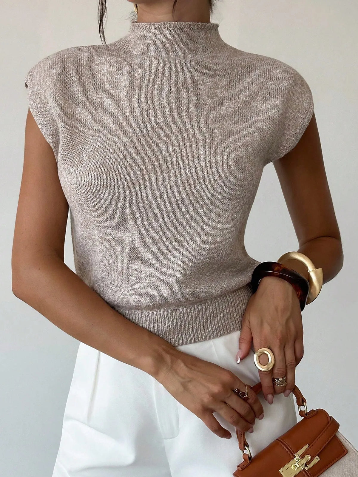 Close view of the beige high-neck knit top with white trousers and a brown handbag