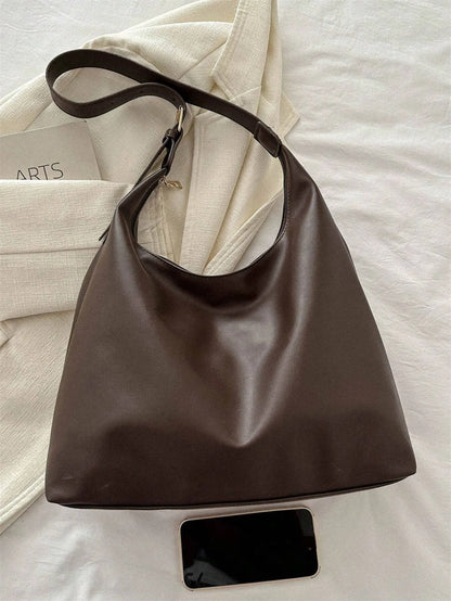 Dark brown slouchy shoulder bag with a single strap, laid flat beside a phone
