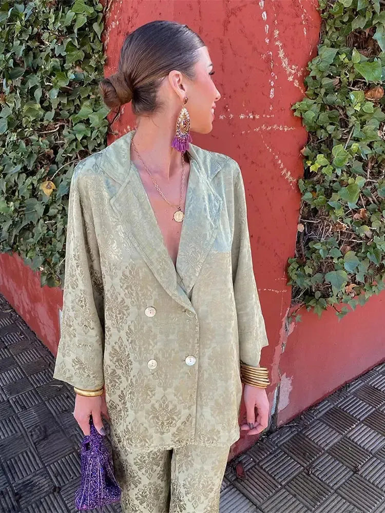 Woman wearing a sage green patterned double-breasted V-neck blazer and matching pants, looking to the side