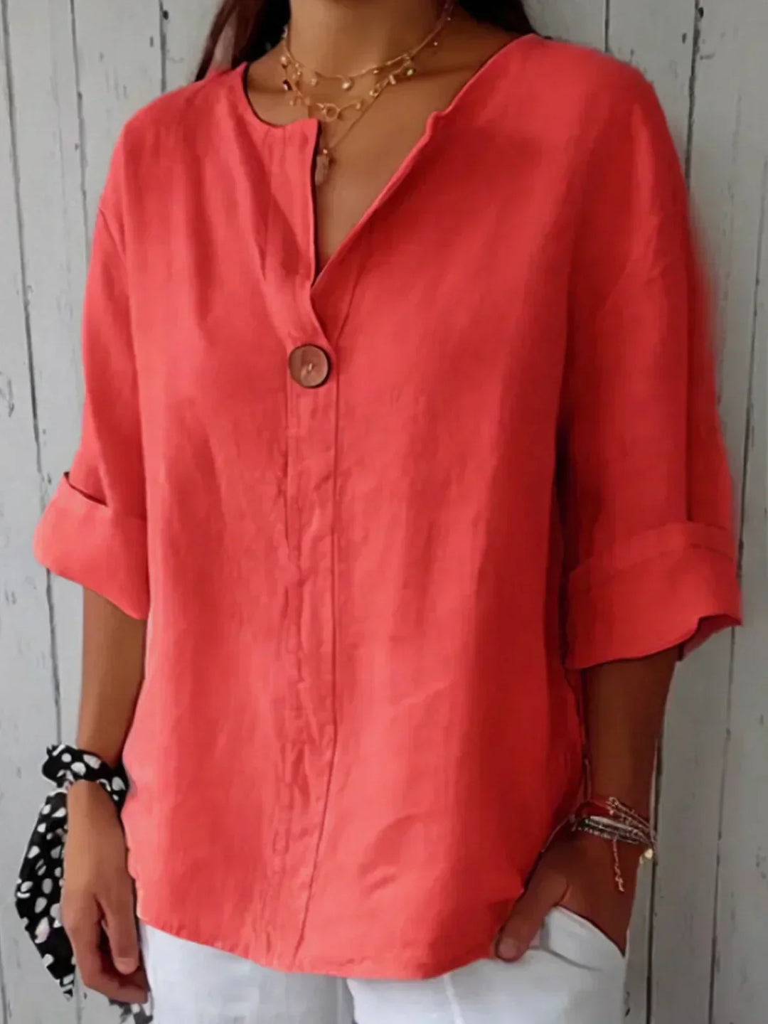 Woman wearing a coral red linen V-neck blouse with a single button and rolled sleeves