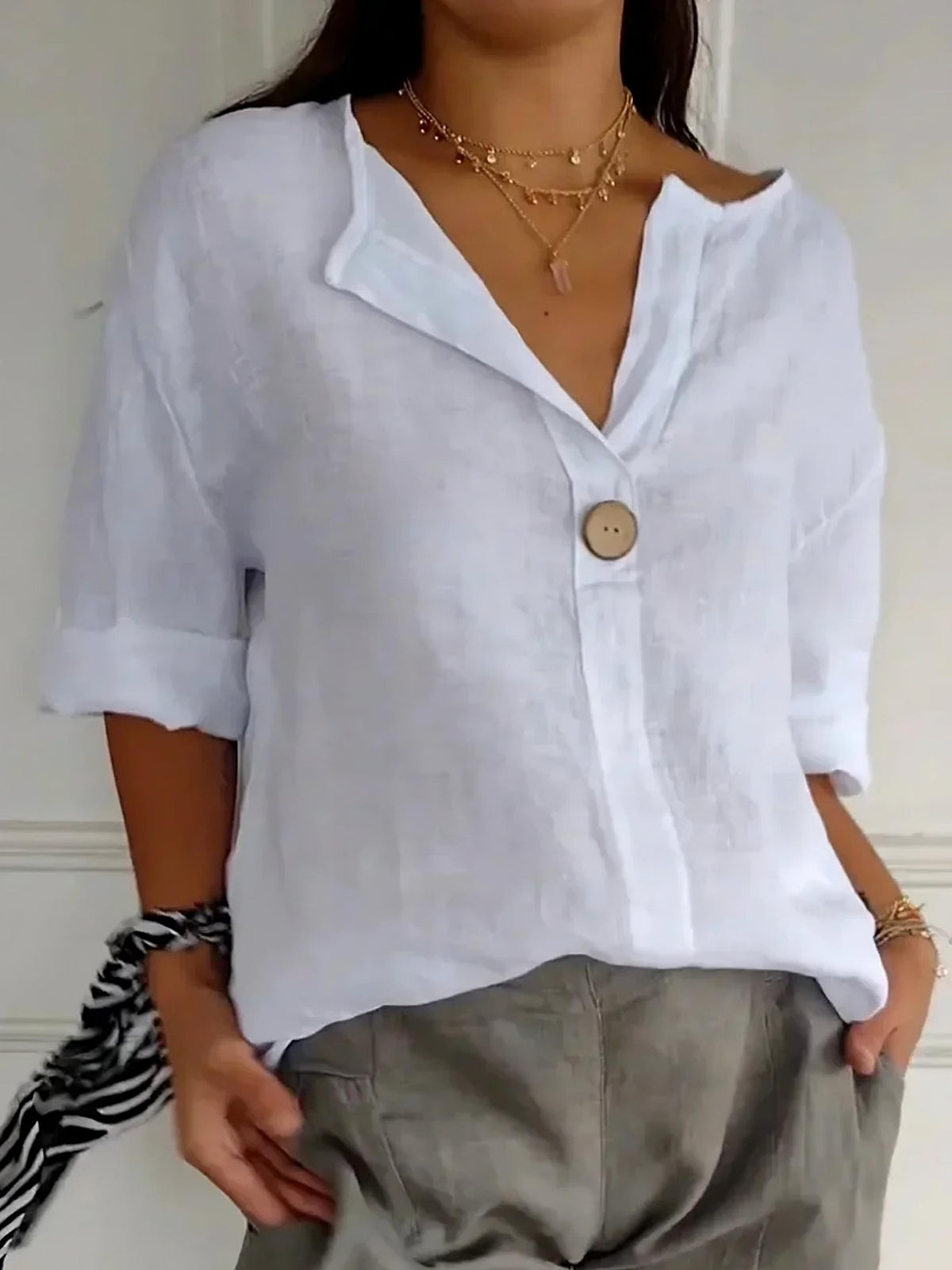 Woman wearing a white linen V-neck blouse with a single button and rolled sleeves
