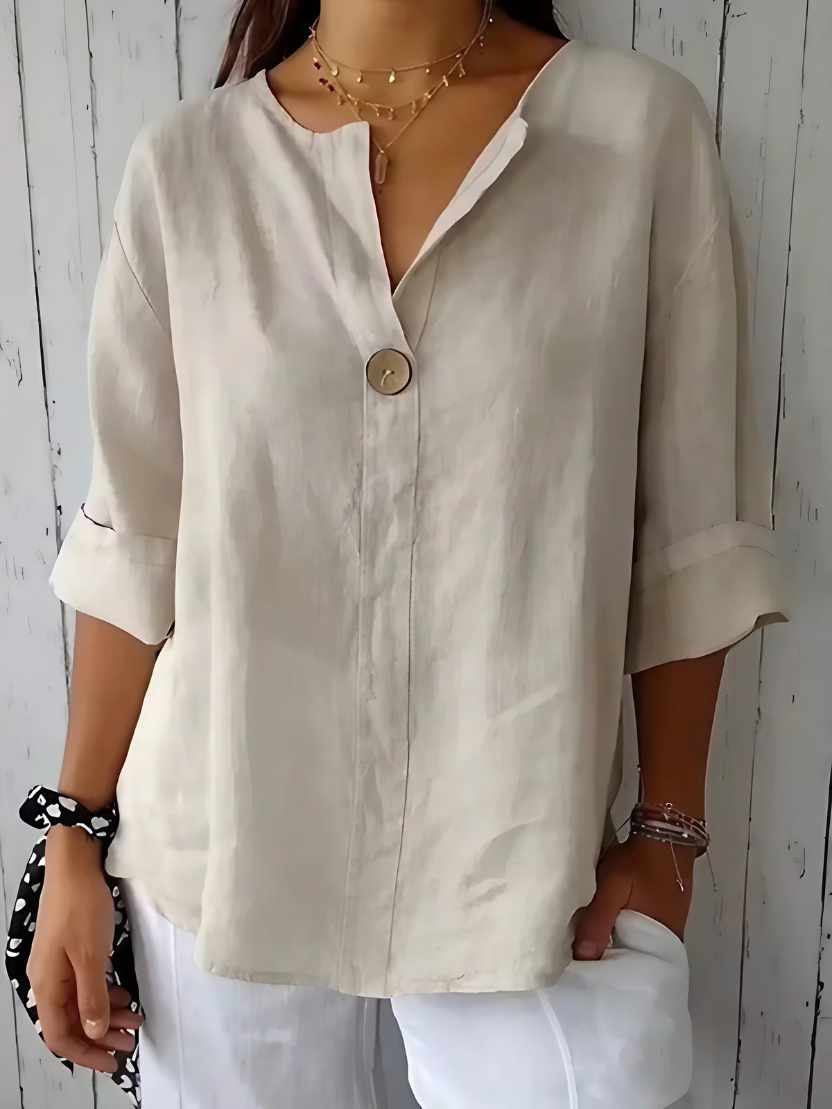 Woman wearing a beige linen V-neck blouse with a single button and rolled sleeves