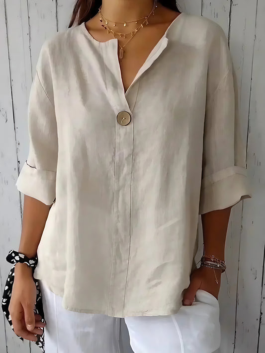 Woman wearing a beige linen V-neck blouse with a single button and rolled sleeves